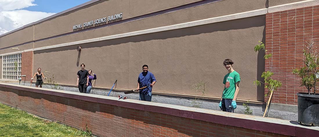 students standing in brick planter in front of a school